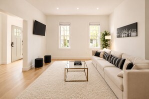 Una sala de estar moderna con un sofá color beige, una mesa de centro de vidrio y dos otomanas negras.