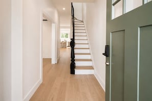 Un pasillo con una escalera, una puerta verde y una zona de cocina al fondo.