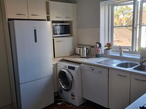 Eine kompakte Küche mit Kühlschrank, Mikrowelle, Toaster, Wasserkocher und Waschmaschine.
