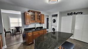 A modern kitchen with wooden cabinets, a granite countertop, a built-in sink, and a wall-mounted washing machine.