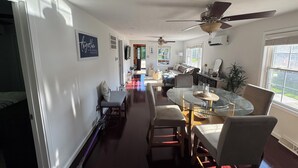 Un vaste espace dédié à la salle à manger, avec une table et des chaises en verre, un ventilateur de plafond et une vue sur l’extérieur.