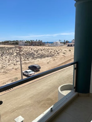 Un balcón con vista a una zona arenosa, una carretera y edificios a lo lejos.