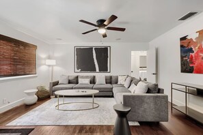 Ein modernes Wohnzimmer mit einem grauen Sofa, einem runden Couchtisch, einer Stehlampe und einem Deckenventilator.
