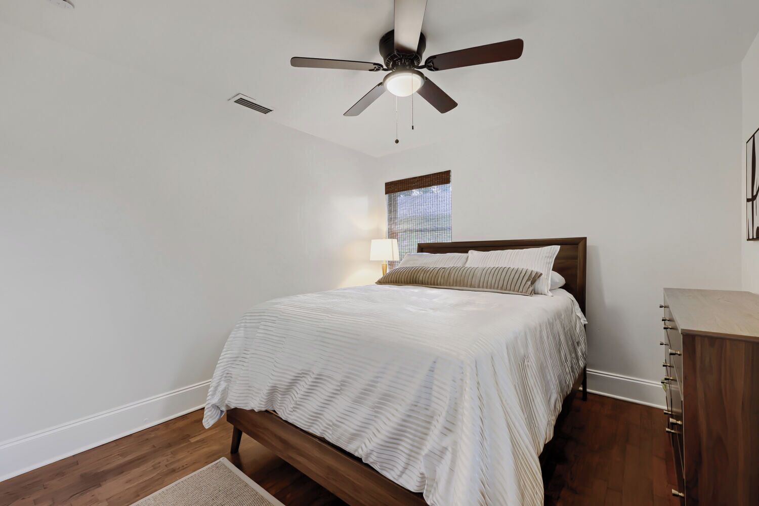 A bedroom with a bed, a ceiling fan, a nightstand, and a dresser.