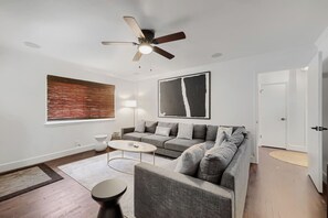 Ein modernes Wohnzimmer mit einem grauen Sofa, zwei runden Couchtischen, einem Deckenventilator und einem großen abstrakten Gemälde.