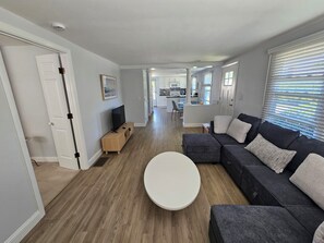 A modern living room with a dark grey sectional sofa, a white coffee table, and a TV on a wooden stand. - Cozy 3 Bedroom Cottage in Charlestown (Charlestown)