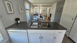 A kitchen with a dishwasher, a sink, and a countertop. There are cabinets and a window with blinds. - Cozy 3 Bedroom Cottage in Charlestown (Charlestown)