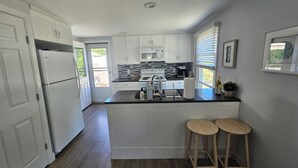A modern kitchen with white cabinets, a black countertop, a built-in stove, and a sink. There are two wooden stools at the island. - Cozy 3 Bedroom Cottage in Charlestown (Charlestown)