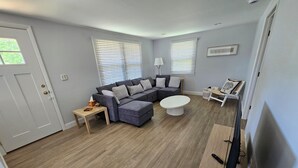 A living room with a sectional sofa, a coffee table, a TV stand, and a door. - Cozy 3 Bedroom Cottage in Charlestown (Charlestown)