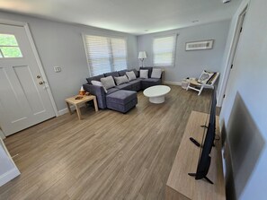 Una sala de estar con un sofá modular, una mesa de centro, un mueble para televisión y una puerta.
