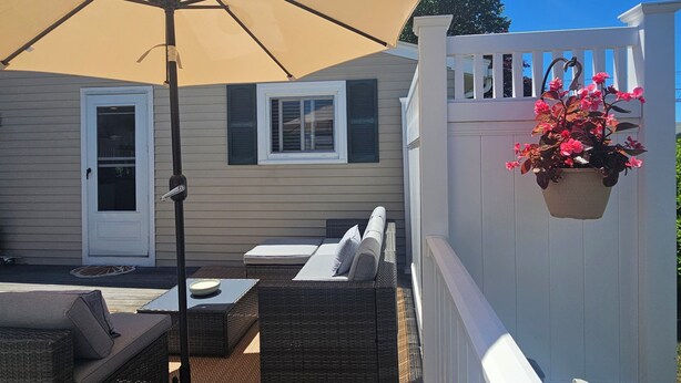 An outdoor patio with a large umbrella, wicker furniture, and a hanging flower pot. - Cozy 3 Bedroom Cottage in Charlestown (Charlestown)