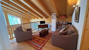 Ein Holzinterieur mit zwei Sofas, einem Fernseher, einem Bücherregal und einem gemusterten Teppich.