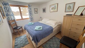 Ein Schlafzimmer mit Bett, einem Holzstuhl, einem Schreibtisch, einem Kleiderschrank und einem Fenster mit Vorhängen.