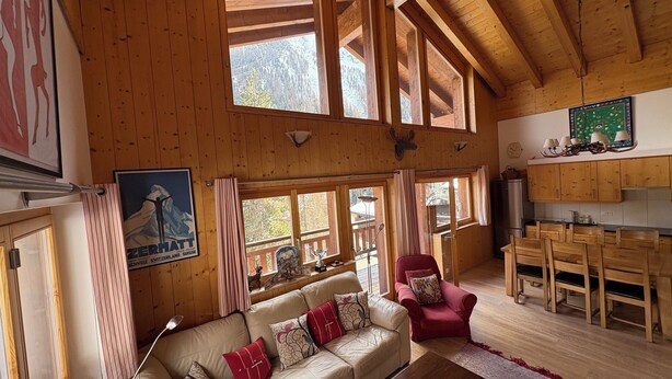 Ein Holzblockhaus-Innenraum mit Sofa, rotem Sessel, Esstisch und Küchenzeile.