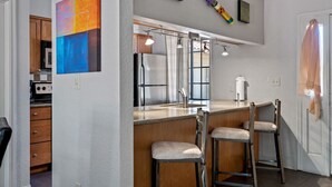 A kitchen with a stainless steel refrigerator, a bar area with stools, and a large window.