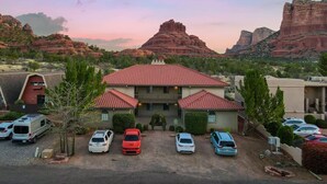 A hotel with a red-tiled roof, a parking lot with several cars, and a mountainous landscape in the background.