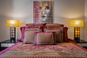 Een bed met meerdere kussens en een groot schilderij erboven.