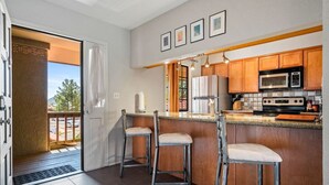 A kitchen with wooden cabinets, a stainless steel refrigerator, a microwave, and a stove. There are two bar stools with cushioned seats. - Toroweap- Sedona Bell Rock Views (Sedona)