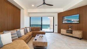A modern living room with a sofa, coffee table, and TV, overlooking a balcony with a view of the sea. - Stunning 3BR 3BA Cortez 601 @ Las Palomas Phase 2 (Puerto Peñasco)