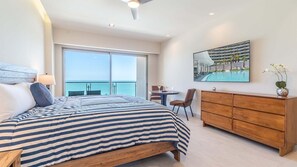 A bedroom with a large bed, a wooden dresser, a desk with a chair, and a large window with a view of the sea. - One 1001-Hotel Room: New Beachfront Resort Offering Luxury & Incredible Views (Puerto Peñasco)