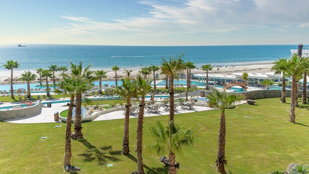 Un resort con varias piscinas, palmeras y vistas a la playa.