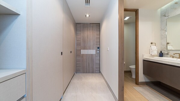 A narrow hallway leading to a bathroom with a modern design, including a wooden door, a sink with a marble countertop, and a mirror. - One 301A Hotel Room: Oceanfront Luxury Suite with Stunning Views (Puerto Peñasco)