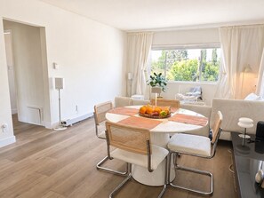 Un comedor moderno con una mesa redonda, sillas, una cesta de frutas y vistas a zonas verdes.