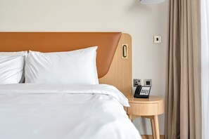 Ein ordentlich bezogenes Bett mit weißen Leinen, ein hölzernes Kopfteil, ein Nachttisch mit Telefon und eine Wandlampe.
