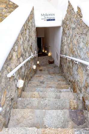 Eine Steintreppe führt zu einem Raum, der ein Schild mit der Aufschrift 'Mykonos The Psarou Dreaming Place' zeigt.