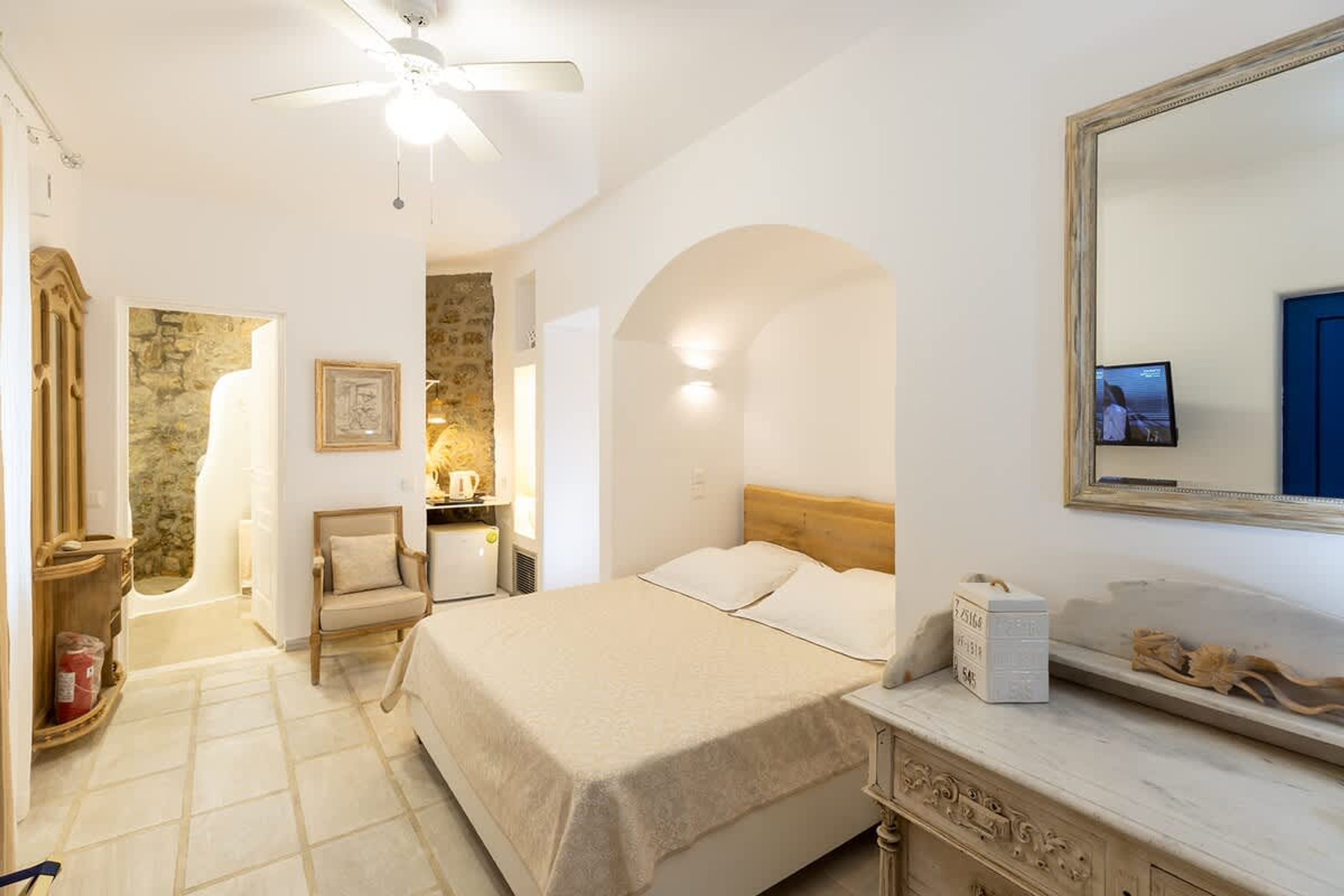 A bedroom with a bed, a chair, a dresser, a mirror, and a ceiling fan.