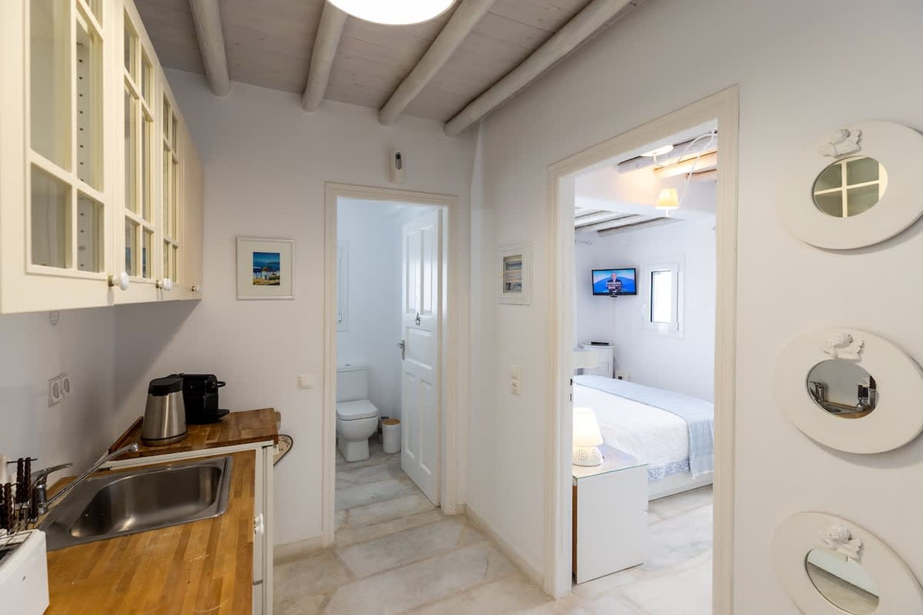 Un couloir étroit mène à une chambre à coucher équipée d’un lit, d’une télévision et d’une salle de bain avec des toilettes et un lavabo.