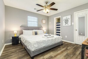Ein Schlafzimmer mit Bett, Deckenventilator, Fenster, Tür und einer Wand mit einem gerahmten Bild.