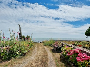A gravel path leading to a body of water, surrounded by flowering plants and a stone wall. - La Grée du Moulin - PEAULE (PEAULE)