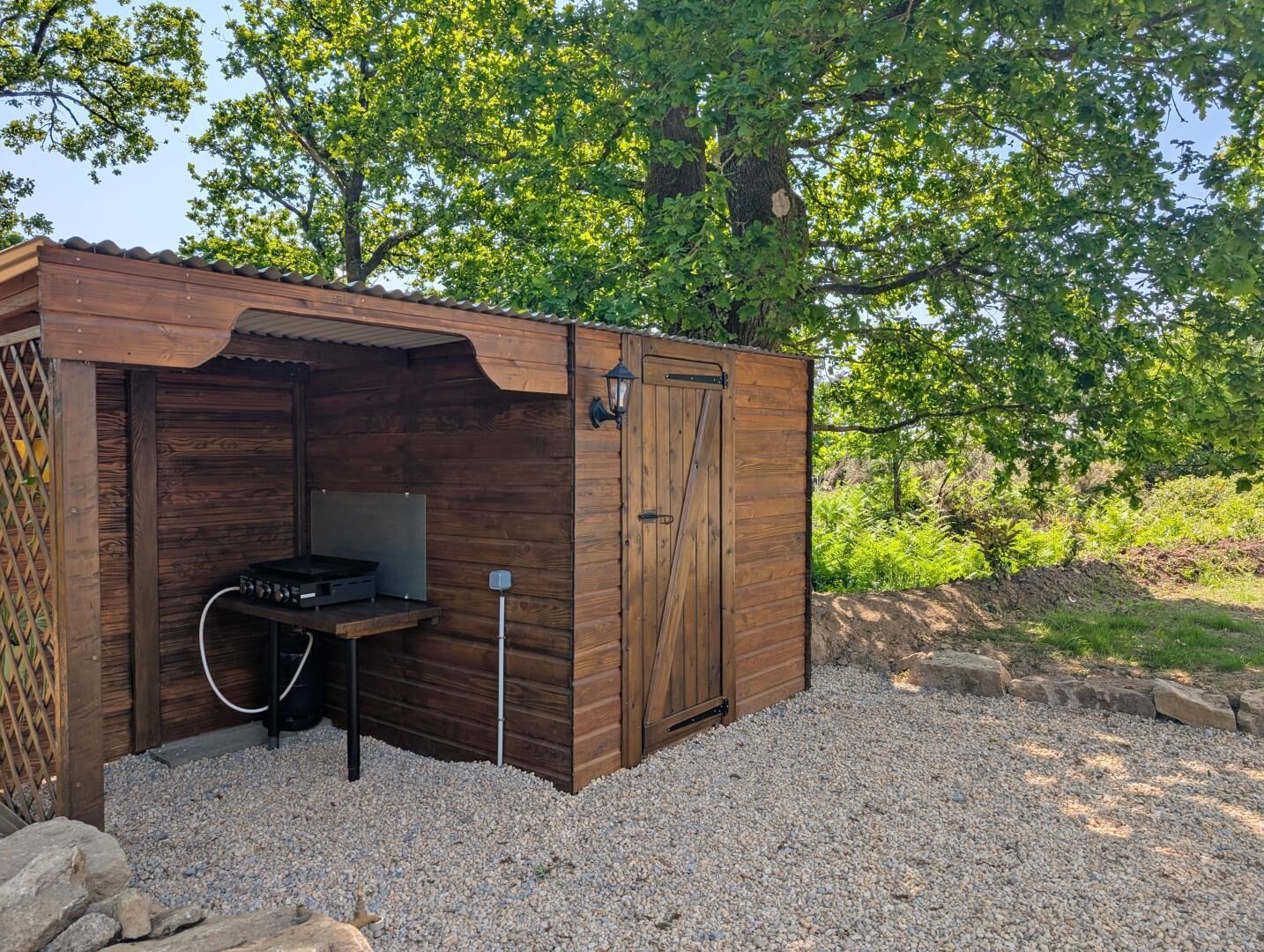 A wooden outdoor structure with a grill, a door, and a light fixture.