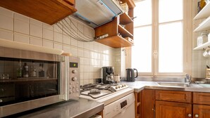 A kitchen with a stove, oven, and dishwasher, wooden cabinets, and a window. - The Haussmann-style Sarcey - Welkeys (Paris)