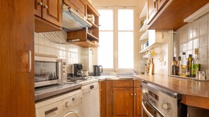A kitchen with wooden cabinets, a washing machine, a microwave, a coffee maker, and a sink. - The Haussmann-style Sarcey - Welkeys (Paris)