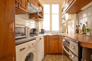 A kitchen with wooden cabinets, a washing machine, a microwave, a coffee maker, and a sink. - The Haussmann-style Sarcey - Welkeys (Paris)