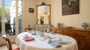 A dining room with a round table set for four, a fireplace, a mirror, and a view of the street outside. - The Haussmann-style Sarcey - Welkeys (Paris)