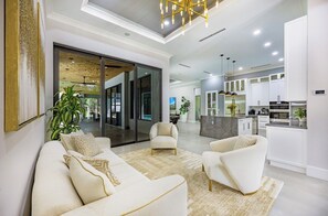 A modern living room with a sofa set, a coffee table, and a dining area with a kitchen in the background. - Private. Polished. Poolside. A Florida Estate That Delivers. (Naples)