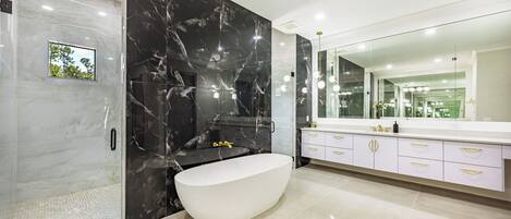 A modern bathroom with a freestanding bathtub, a large mirror, and a vanity with gold handles.