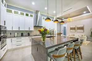 Une cuisine moderne avec des meubles blancs, un îlot central doté de tabourets et des luminaires suspendus.