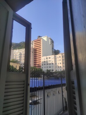 A view through a window with a metal fence, a building with multiple floors, and a clear sky. - Comfortable and convenient apartment in Copacabana. (Rio de Janeiro)