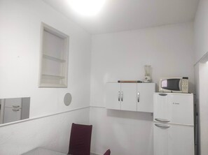 Une petite pièce blanche, avec un meuble blanc, un four à micro-ondes et un réfrigérateur.