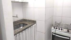 Ett litet kök med en bänkskiva i granit, en diskho i rostfritt stål, en vit gasspis och vita kakelväggar.