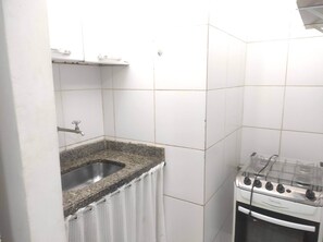 A small kitchen with a granite countertop, a stainless steel sink, a white gas stove, and white tiled walls. - Comfortable and convenient apartment in Copacabana. (Rio de Janeiro)