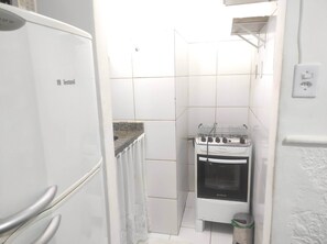 A compact kitchen with a white refrigerator, a stove, and a trash bin. - Comfortable and convenient apartment in Copacabana. (Rio de Janeiro)