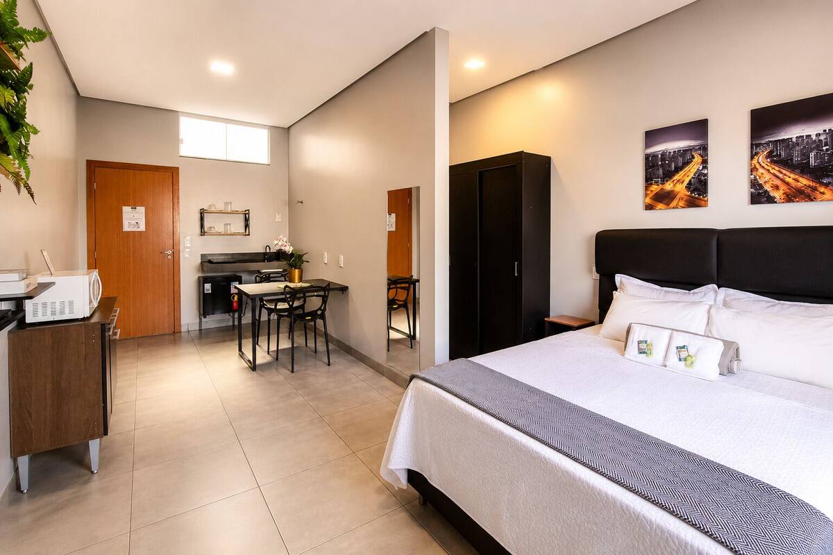 A hotel room with a bed, a desk, a chair, a small kitchen area, and a closet.