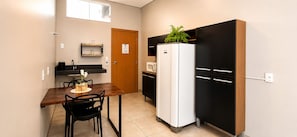 A compact kitchen with a wooden table, black chairs, a white refrigerator, and a microwave.