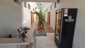 Corredor de hotel com um balcão de recepção, uma placa SmartHome e uma planta.