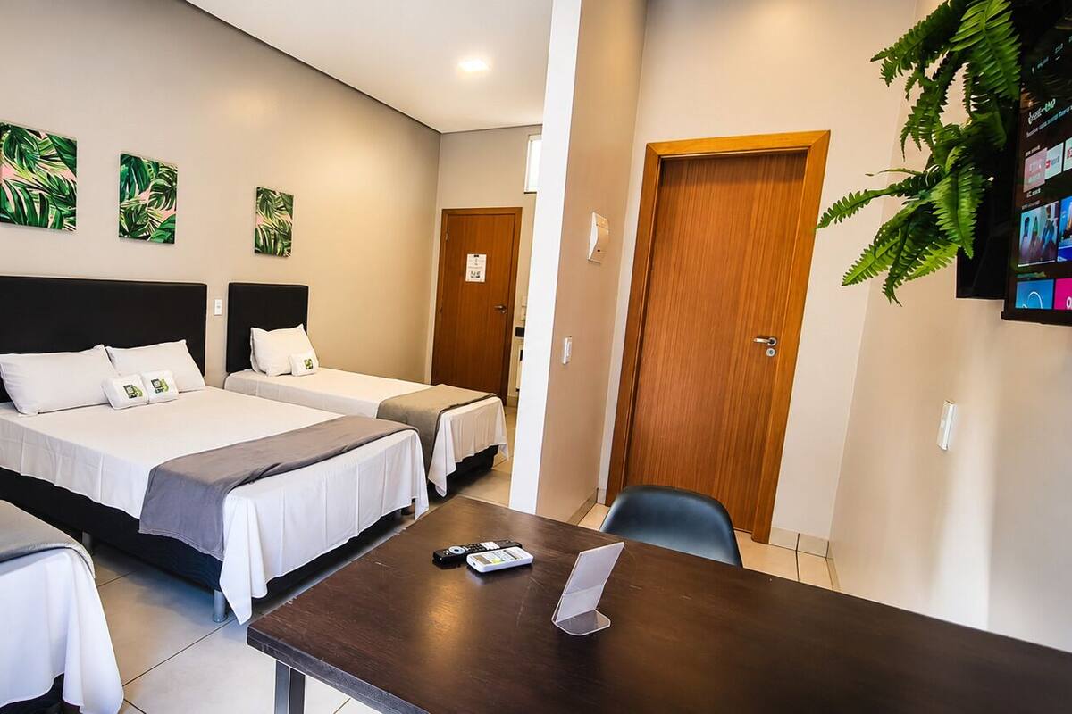 A hotel room with three beds, a wooden desk, and a TV mounted on the wall.